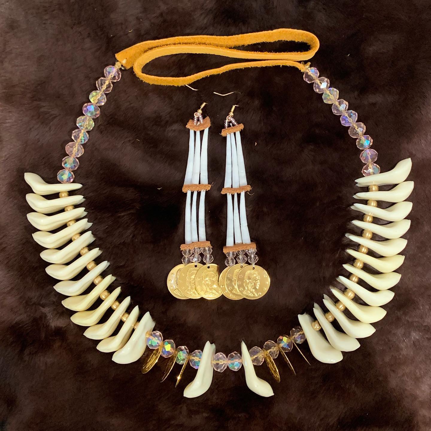 This imitation elk tooth necklace features pink glass beads, brass beads, brass coins, and a hide strap.Matching two-tiered dentalium earrings feature pink mini glass beads, brass coins, and brass hardware.